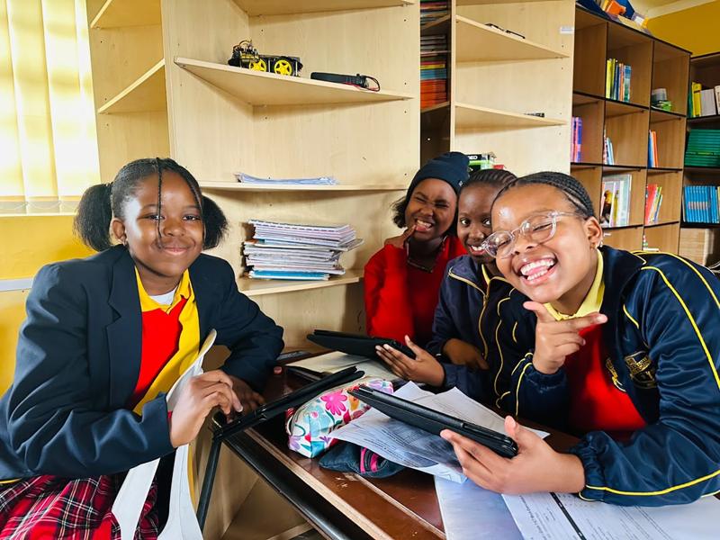Pupils with a tablet beside the bookshelves